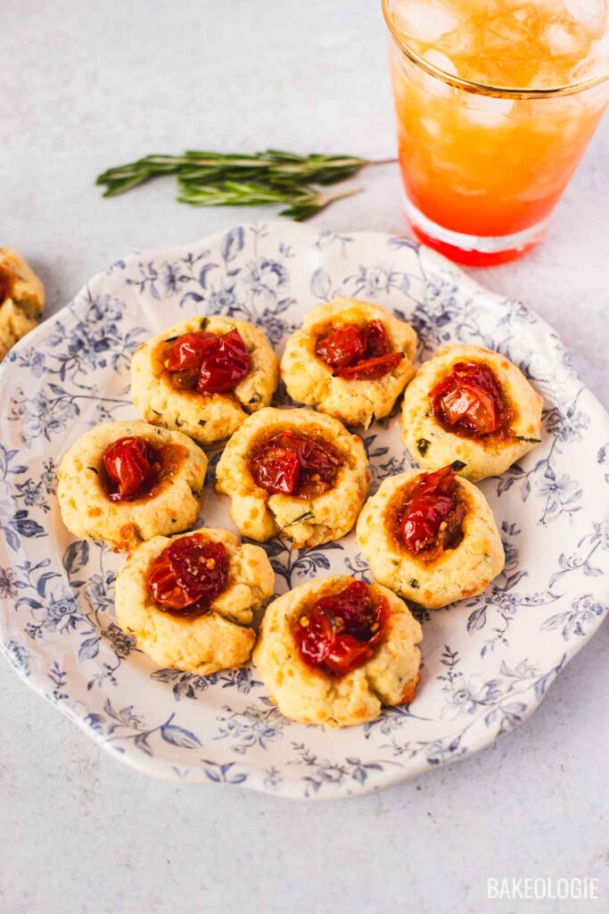 Close-up of herbed cheese thumbprint cookies with tomato jam centers, styled as a savory appetizer with a cocktail.
