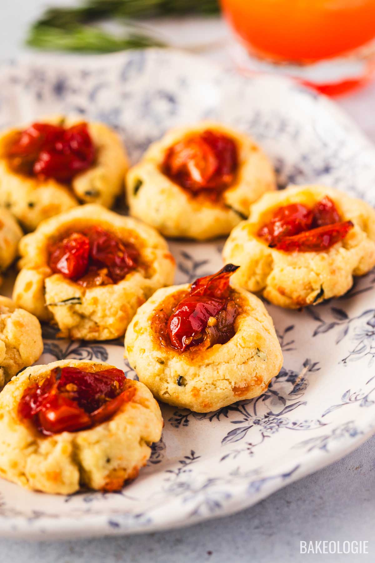 Close-up of herbed cheese thumbprint cookies filled with tomato jam, showing the crumbly cheese texture and glossy jam topping.