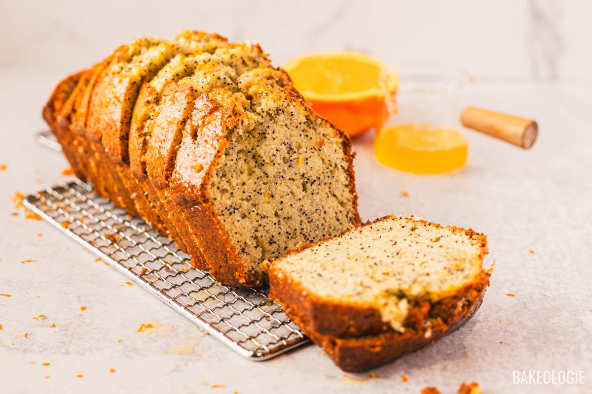 Orange poppyseed loaf cake on a wire rack with a sliced piece in front