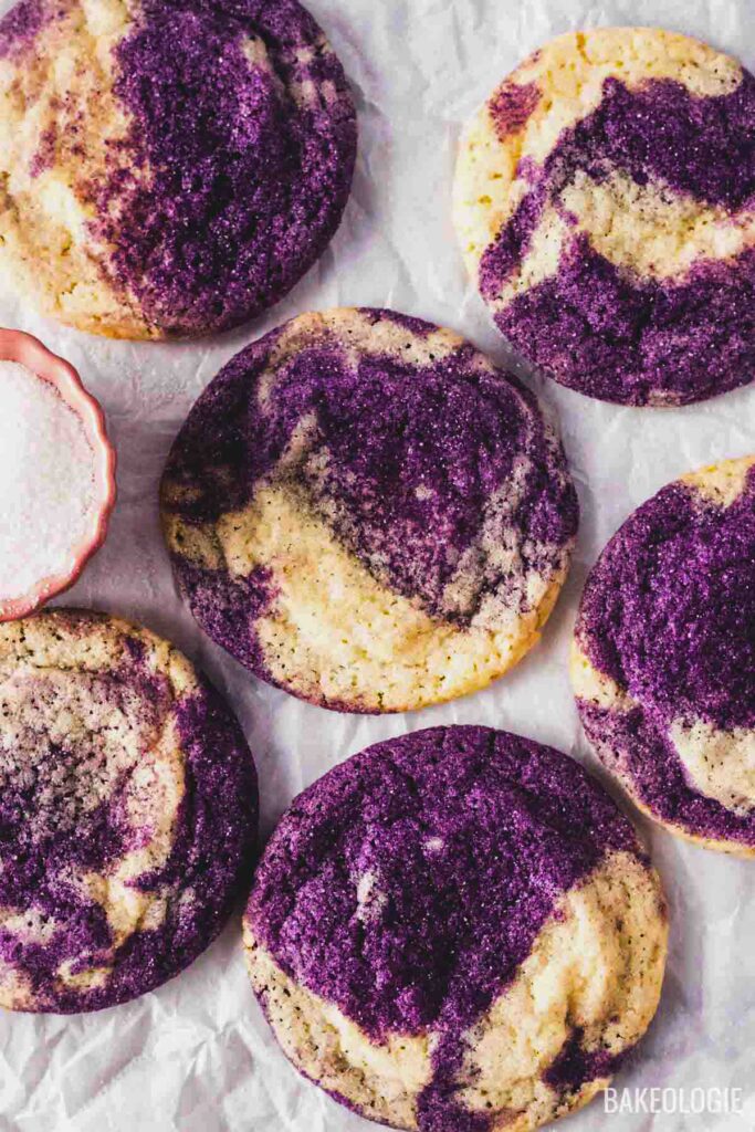 Marbled ube sugar cookies on parchment paper with a small bowl of granulated sugar