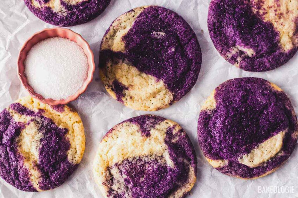 Marbled ube sugar cookies on parchment paper with a small bowl of granulated sugar