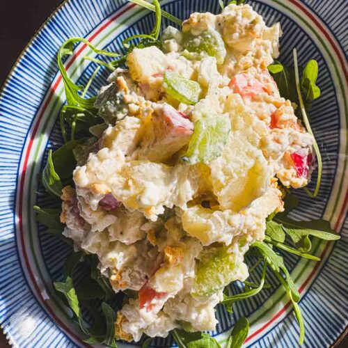Korean potato salad (gamja salad) served on a plate with arugula, featuring creamy mashed potatoes with apples, carrots, cucumber, and egg