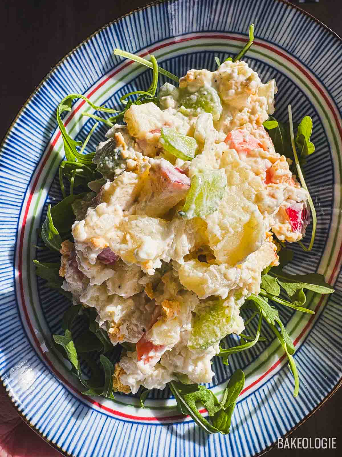 Korean potato salad (gamja salad) served on a plate with arugula, featuring creamy mashed potatoes with apples, carrots, cucumber, and egg