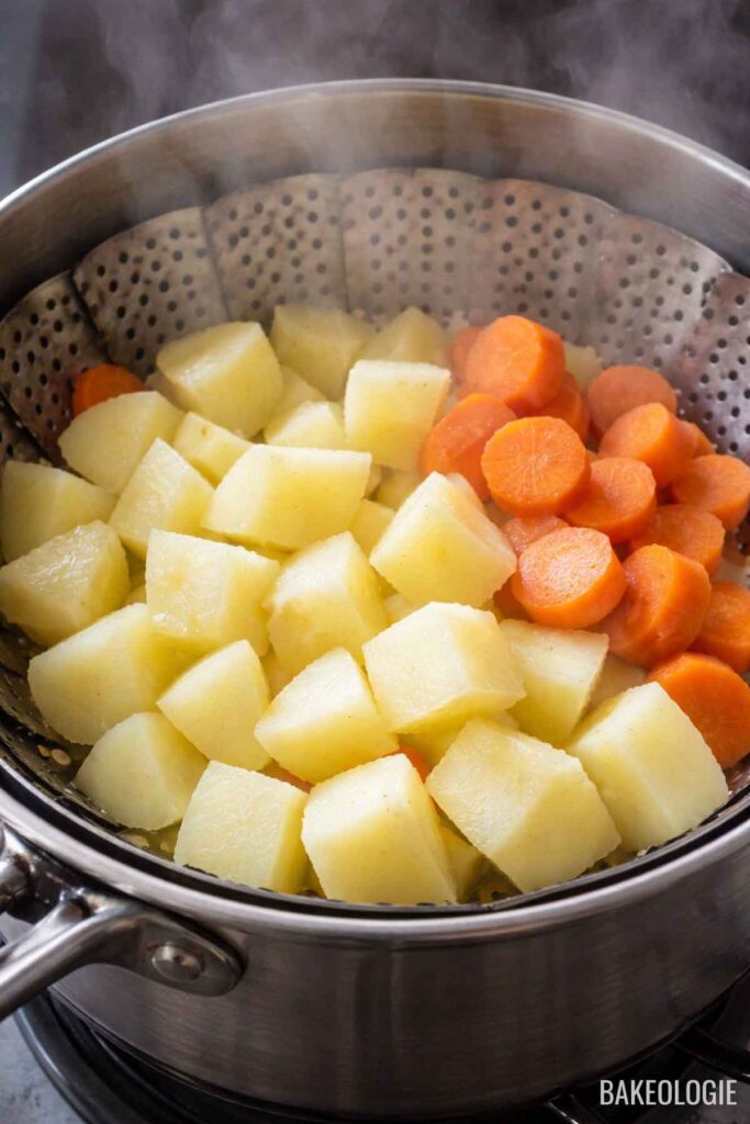 Steaming cubed potatoes and sliced carrots in a pot until fork-tender