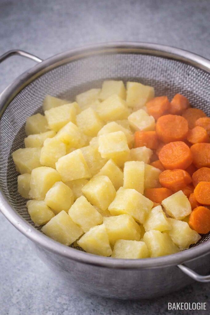 Cooked potatoes and carrots draining in a colander and cooling slightly