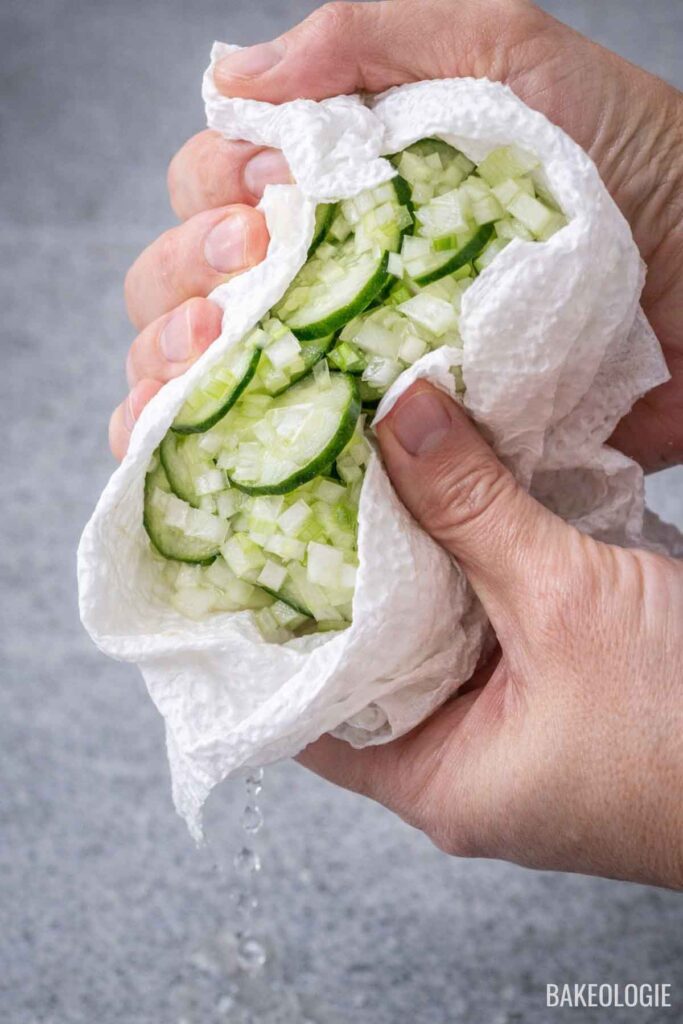 Hands squeezing salted cucumber and onion in paper towels to remove excess water