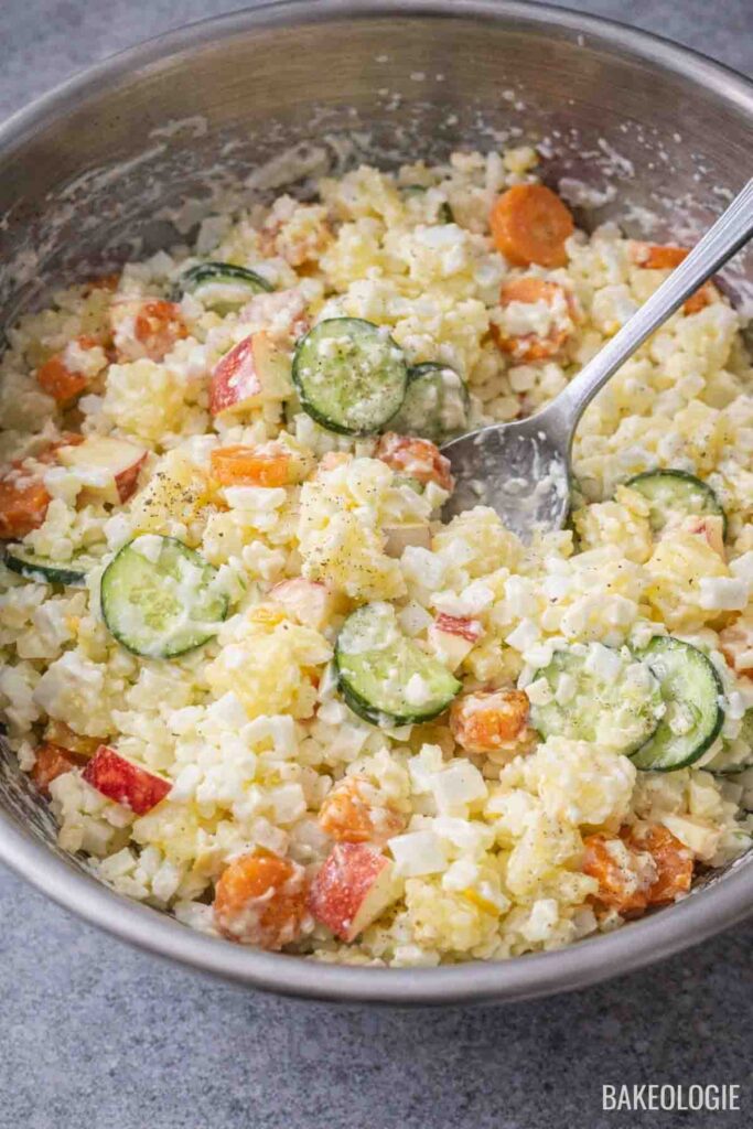 Mixing potatoes, carrots, cucumber, onion, apple, and mayonnaise in a bowl
