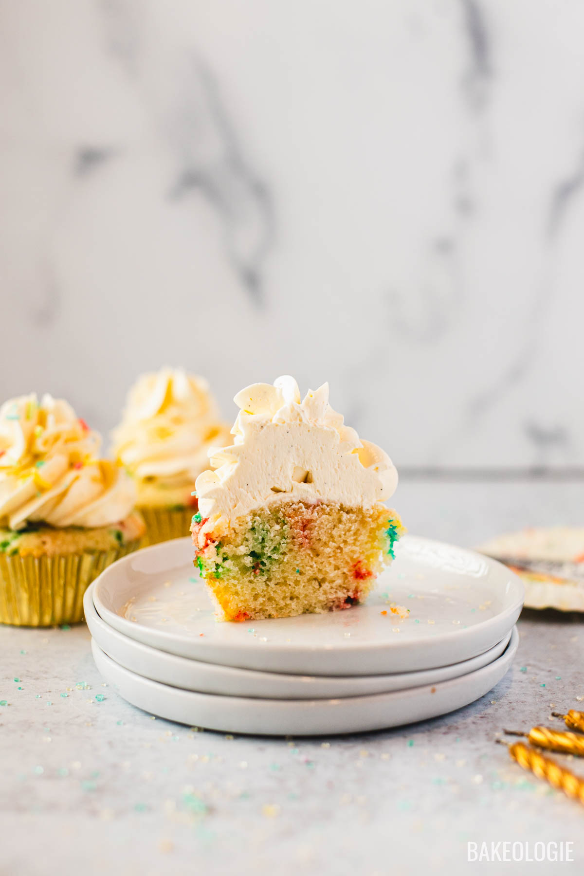 Vanilla sprinkle cupcake cut in half showing soft crumb and Swiss meringue buttercream frosting