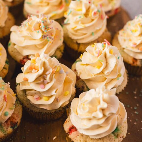 Homemade cupcakes with Swiss meringue buttercream frosting and rainbow sprinkles arranged on a wooden serving board