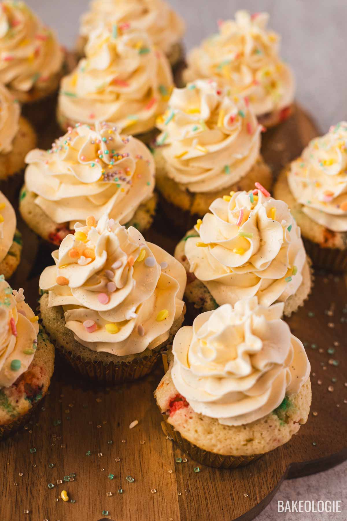 Homemade cupcakes with Swiss meringue buttercream frosting and rainbow sprinkles arranged on a wooden serving board