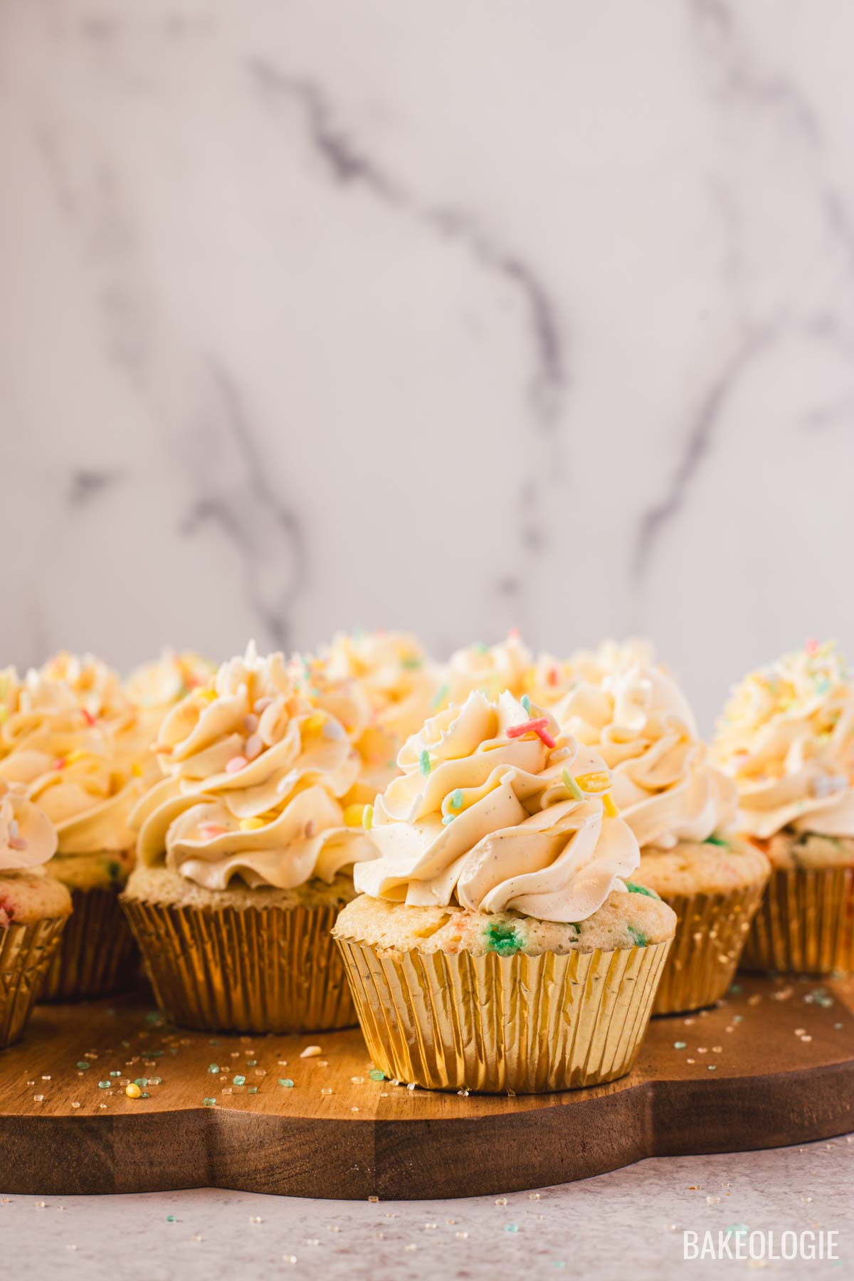 Vanilla cupcakes with Swiss meringue buttercream topped with colorful sprinkles on a wooden board