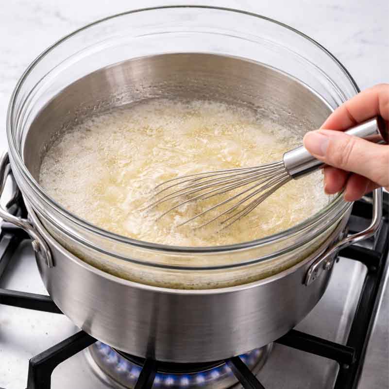 Whisking egg whites and sugar over a double boiler until dissolved and heated