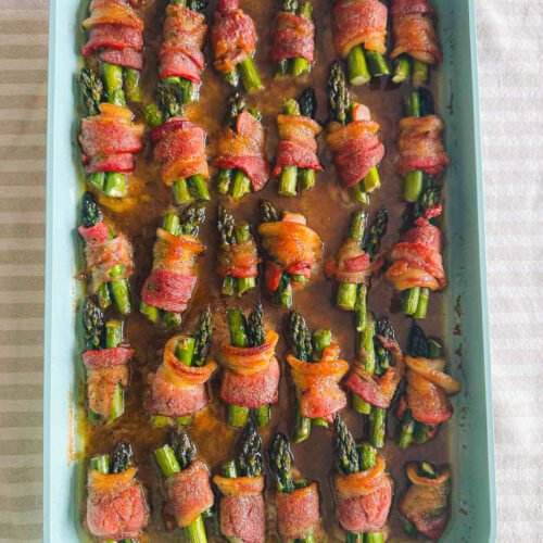 Oven-baked bacon-wrapped asparagus bundles in a baking dish with a brown sugar glaze.
