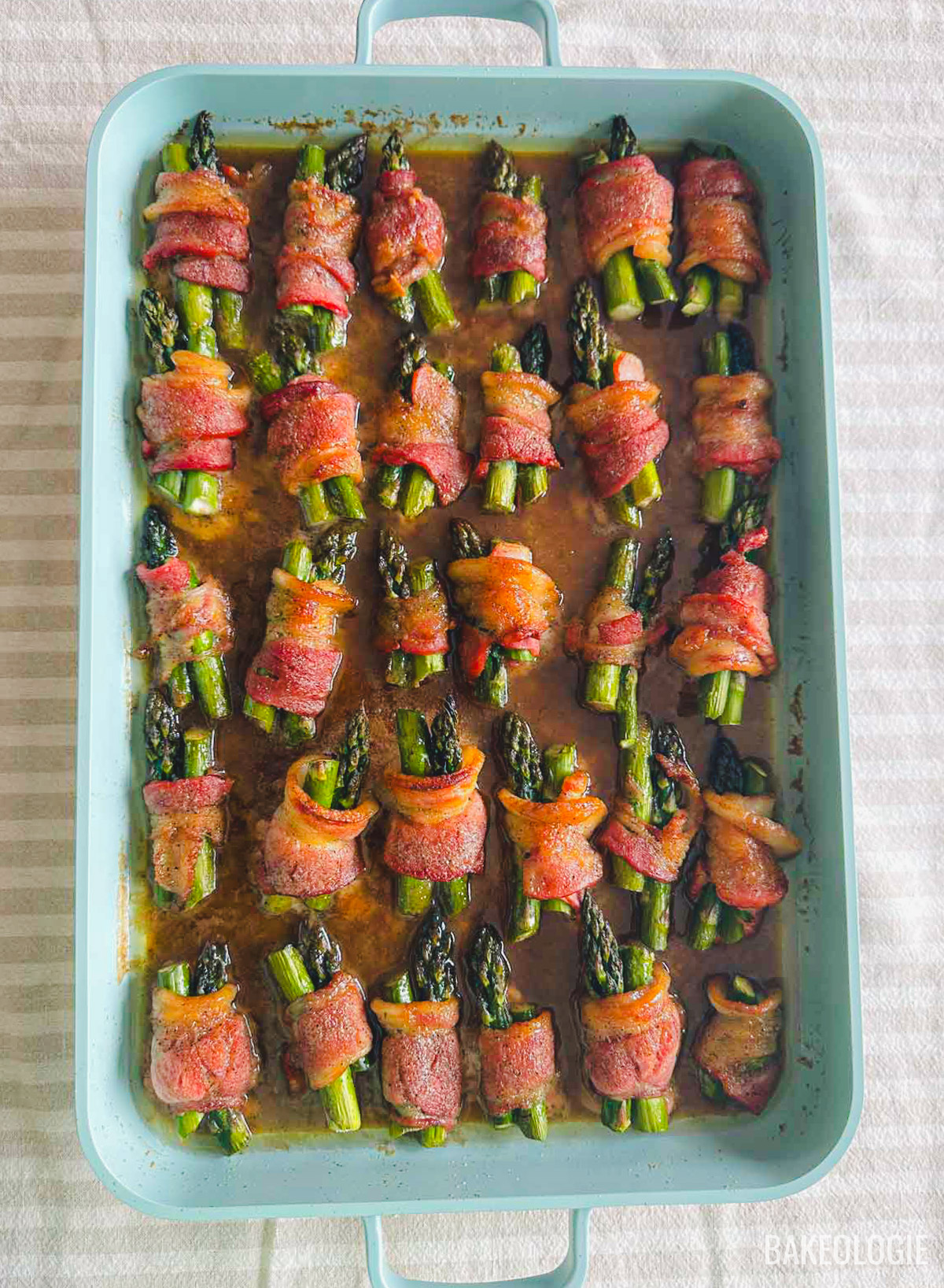 Oven-baked bacon-wrapped asparagus bundles in a baking dish with a brown sugar glaze.