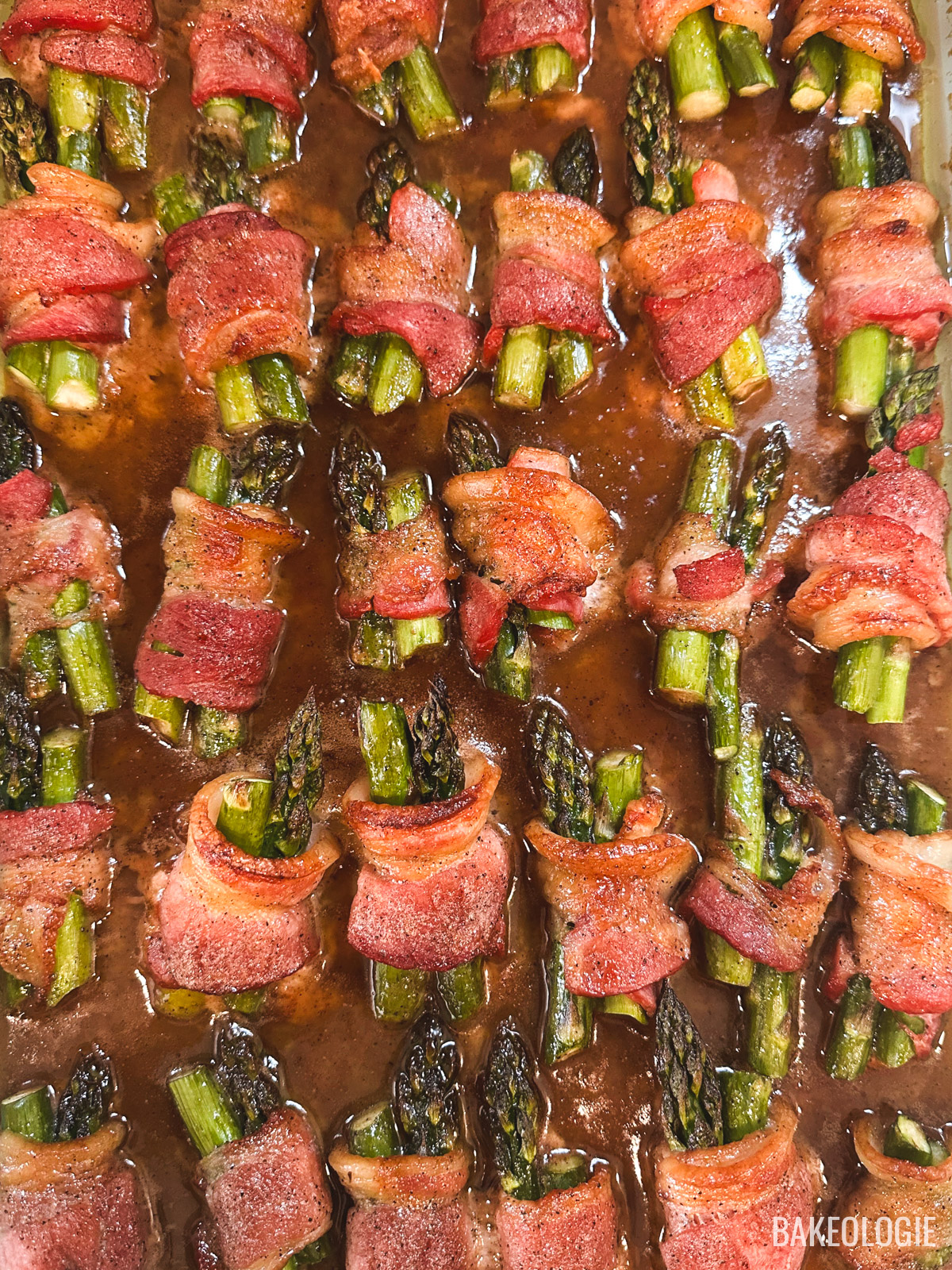 Oven-baked bacon-wrapped asparagus bundles in a baking dish with a brown sugar glaze.
