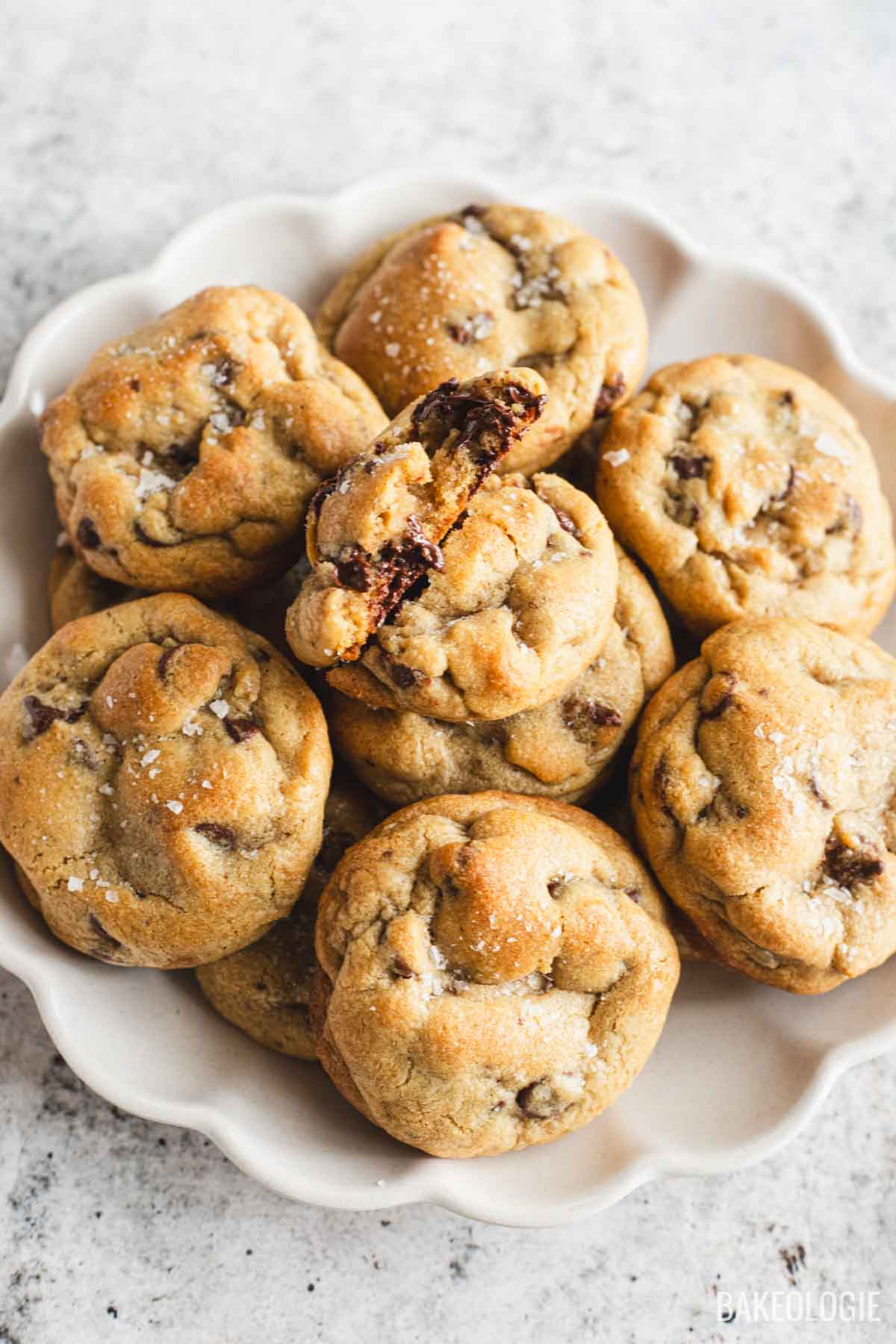 Stack of chewy chocolate chip cookies with flaky sea salt and melted chocolate chunks on a white serving plate.