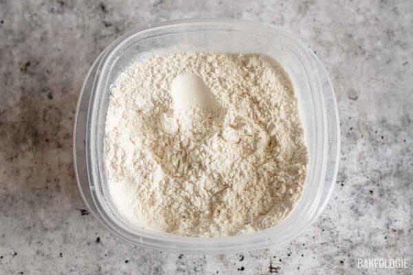 Measured flour, baking soda, cornstarch, and salt in a container, ready to be whisked together for cookie dough.