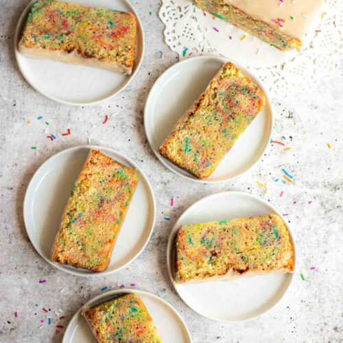 Funfetti Sour Cream Pound Cake slices with vanilla glaze and rainbow sprinkles arranged on white plates.