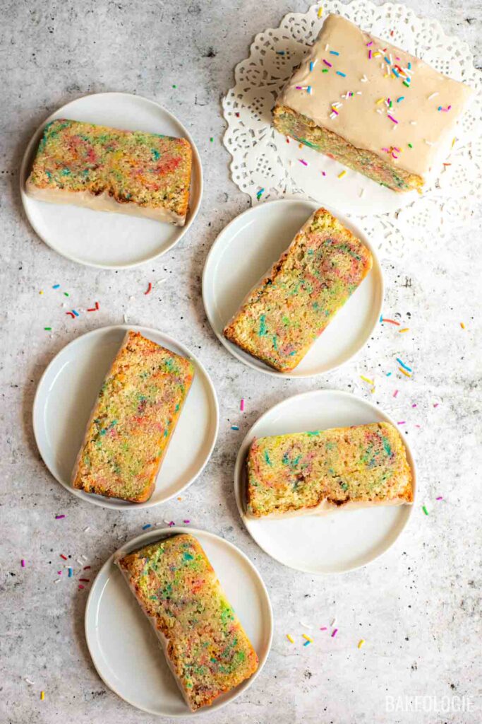 Funfetti Sour Cream Pound Cake slices with vanilla glaze and rainbow sprinkles arranged on white plates.