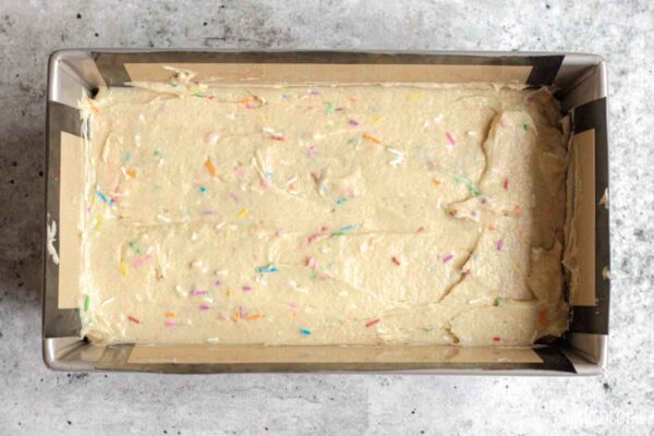 Funfetti Sour Cream Pound Cake batter spread evenly in a prepared loaf pan before baking.