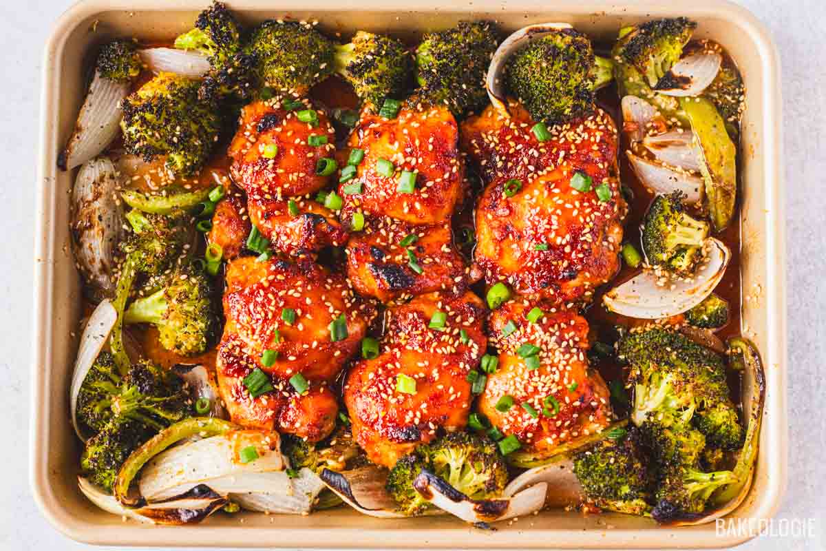 Honey gochujang chicken thighs baked with roasted broccoli and onions, topped with sesame seeds and sliced green onions.