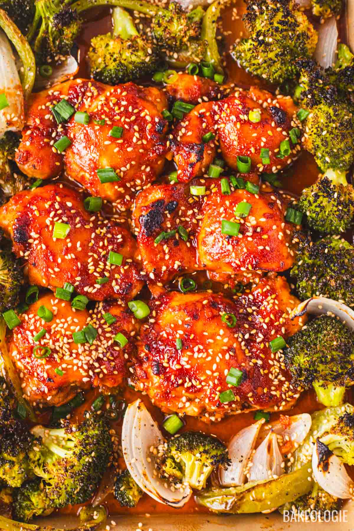 Honey gochujang chicken thighs baked with roasted broccoli and onions, topped with sesame seeds and sliced green onions.