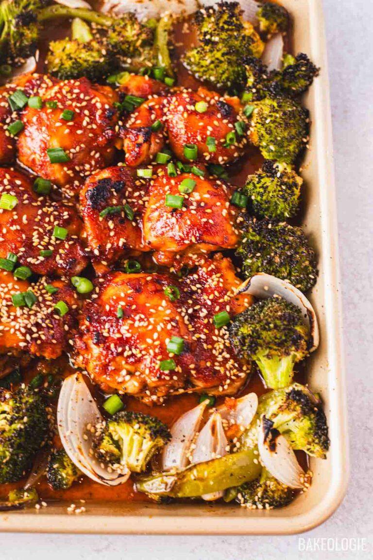 Honey gochujang chicken thighs baked with roasted broccoli and onions, topped with sesame seeds and sliced green onions.