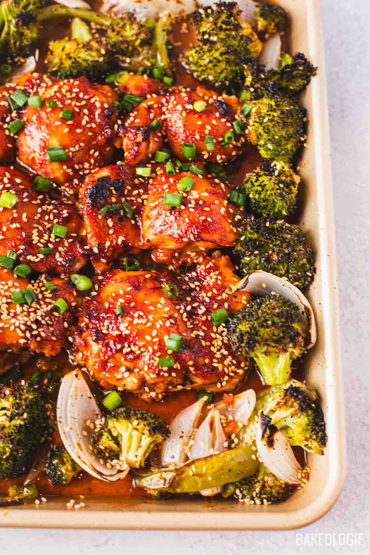 Honey gochujang chicken thighs baked with roasted broccoli and onions, topped with sesame seeds and sliced green onions.