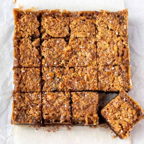 Overhead view of pecan pie brownies cut into squares on parchment, with one square moved aside.