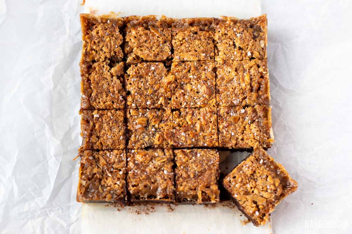 Overhead view of pecan pie brownies cut into squares on parchment, with one square moved aside.