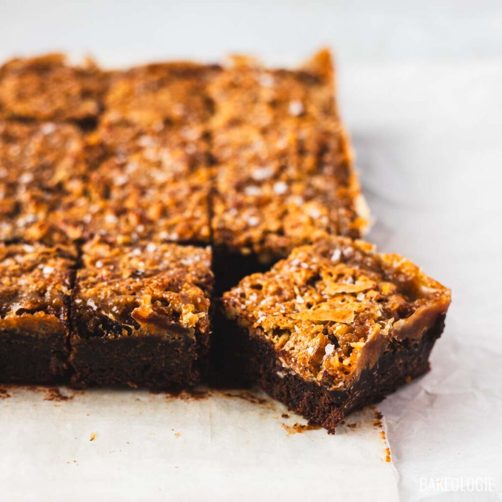 Pecan pie brownie squares with golden pecan topping and one square pulled forward.