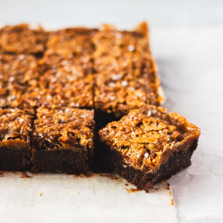 Pecan pie brownie squares with golden pecan topping and one square pulled forward.